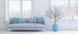A contemporary living room featuring a white couch adorned with blue pillows, situated near a large window. The space is minimalistic and stylish, with vases adding a touch of decoration.