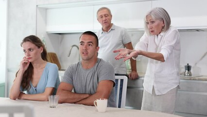 Wall Mural - Portrait of an offended married couple in a home kitchen, which mature family members reprimand. Family conflict