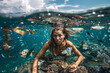 A woman is swimming in the ocean with a lot of fish around her. The water is murky and there is trash floating around her