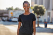A joyful African American woman in a long black Tee - black t-shirt mockup - blurred city background - fashion posture	
