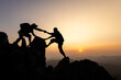 © Tinnakorn - silhouette of Teamwork of two men hiker helping each other on top of mountain climbing team. Teamwork friendship hiking help each other trust assistance silhouette in mountains, sunrise.