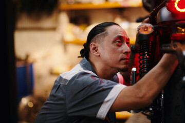 Wall Mural - Concentrated mechanic examining broken motorcycle in workshop