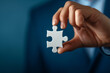 Close-up of Businessman's Hand Holding a Single Puzzle Piece on Blue Background