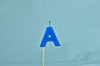 close up on a blue letter A birthday candle with fire on a white background.
