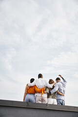 back view of group of young multicultural friends in casual urban attires posing on rooftop