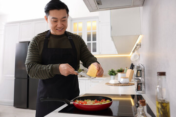 Wall Mural - Cooking process. Man grating cheese into frying pan in kitchen