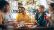© Gorodenkoff - Diverse Group of Friends Enjoying Leisure Time in a Street Cafe. Young Women and Men Sitting Behind a Table, Having Fun and Joyful Conversations. Black African Girl Sharing Motivational Work Stories