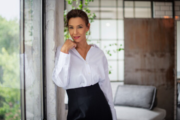 Wall Mural - Portrait of a brunette haired woman standing at the window and smiling to the camera