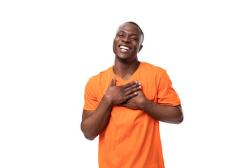 Wall Mural - young african guy dressed in an orange t-shirt smiling cutely and experiencing happiness on a white background with copy space