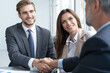 © opolja - Handshake in agreement against young business people in board room meeting.