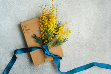 Gift Box With Mimosa Flowers And Blue Ribbon On Stone Background