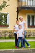 Woman and two boys stand in front of house on grassy lawn