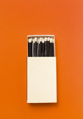 Black matches in a box on a orange background.