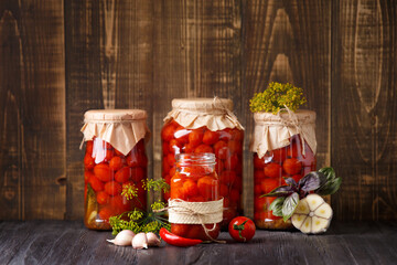 Wall Mural - Pickled cherry tomatoes in jars and spices on a wooden background, copy space.
