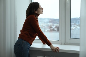 Poster - Sad young woman near window indoors, space for text