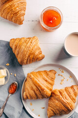 Plate with two fresh croissants, jam and coffee on white wooden table. Top view.