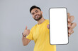 © New Africa - Happy man holding smartphone with empty screen and showing thumbs up on grey background, space for text