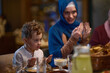 © .shock - In a modern restaurant setting, a European Islamic family comes together for iftar during Ramadan, engaging in prayer before the meal, uniting tradition and contemporary practices in a celebration of