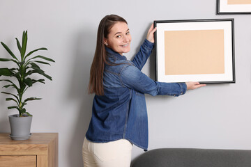 Wall Mural - Woman hanging picture frame on gray wall at home