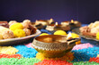 Diwali celebration. Diya lamps and colorful rangoli on table against violet background, closeup