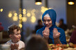© .shock - In a modern restaurant setting, a European Islamic family comes together for iftar during Ramadan, engaging in prayer before the meal, uniting tradition and contemporary practices in a celebration of