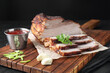 Pieces of baked pork belly served with sauce and parsley on black textured table, closeup