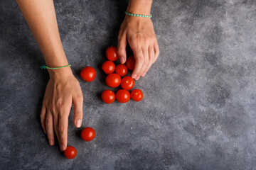 Woman hands with ripe tomatoes cherry on the gray table background, closeup. Handful of fresh red little tomatoes in female hands. Healthy snack and healthy eating, vegan and vegetarian food, top view