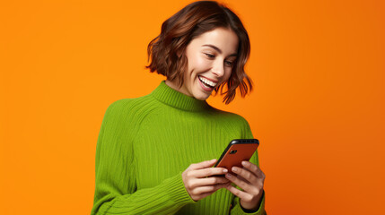 Wall Mural - Happy smiling young woman is using her smartphone against orange background