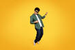 Cool african american guy playing invisible guitar, yellow background
