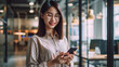 © MP Studio - Smiling woman looking at her smartphone, standing in a modern office