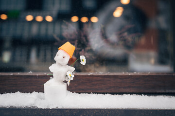 A small snowman with a chamomile flower on the windowsill of a street cafe.