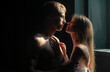 Romantic couple in love looking at each other, embracing and kissing in bedroom on black background.