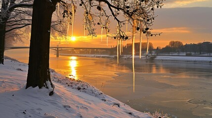 Sticker - the sun is setting over a river with ice on the water and trees in the foreground and a bridge in the background.