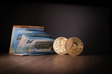 2 Bitcoin coins are next to a bundle of euro banknotes