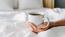 hand s of young woman with coffee mug in bed with white linens minimal happy morning concept
