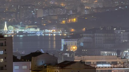 Wall Mural - Aerial view of Lisboa downtown night timelapse. Panoramic of Baixa, Rossio and Chiado rooftops from above. Illuminated buildings. Almada on the other side of Tejo river. Portugal