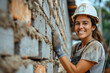 © Duckai - Builder and bricklayer with copy space on a brick and cement wall, woman working with a smile and enterprising