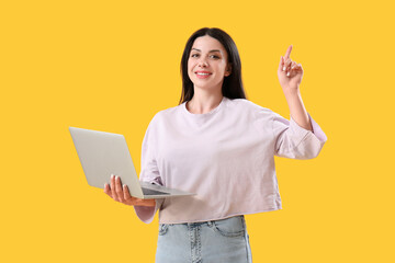 Female programmer with laptop pointing at something on yellow background