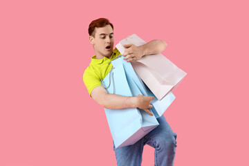 Canvas Print - Shocked young man with shopping bags on pink background