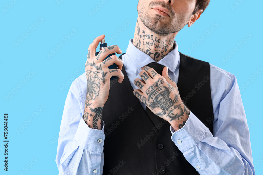 Tattooed young man applying perfume on blue background, closeup