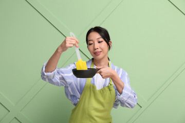 Poster - Portrait of young Asian woman with frying pan and spatula on green background