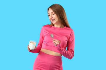 Poster - Sporty young woman with tasty yoghurt on blue background