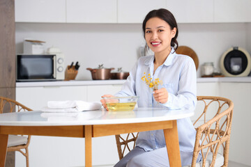 Wall Mural - Young Asian woman preparing steam inhalation with herbs at table in kitchen