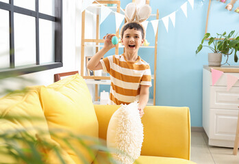 Sticker - Surprised little boy in bunny ears found Easter egg behind cushion at home