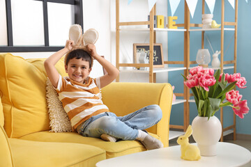 Sticker - Cute little boy with bunny ears sitting on sofa at home. Easter celebration