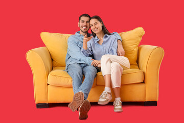 Sticker - Beautiful young happy couple watching TV on sofa against red background