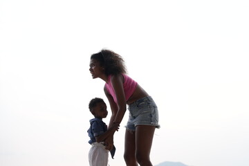 Wall Mural - Mixed race African and Asian mother and boy is playing at the outdoor area. smiling happy family have fun running on the beach. portrait of mom and kid lifestyle with a unique hairstyle.