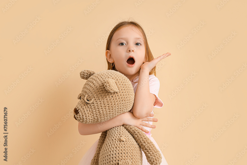 Shocked little girl with teddy bear on beige background