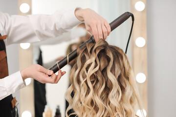 Wall Mural - Hair styling. Hairdresser curling woman's hair in salon, closeup