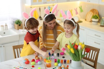 Sticker - Easter celebration. Mother and her cute children with bunny ears painting eggs at white marble table in kitchen